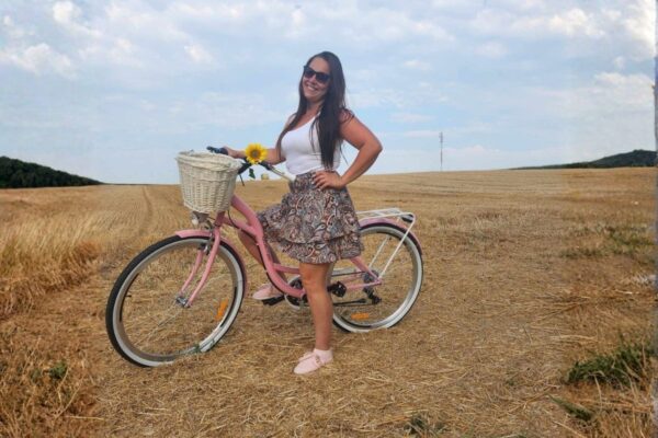 Nainen seisoo vaaleanpunaisen pyörän vieressä pellolla.