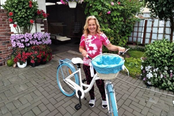 Nainen pyörän ja kukkien kanssa pihalla.