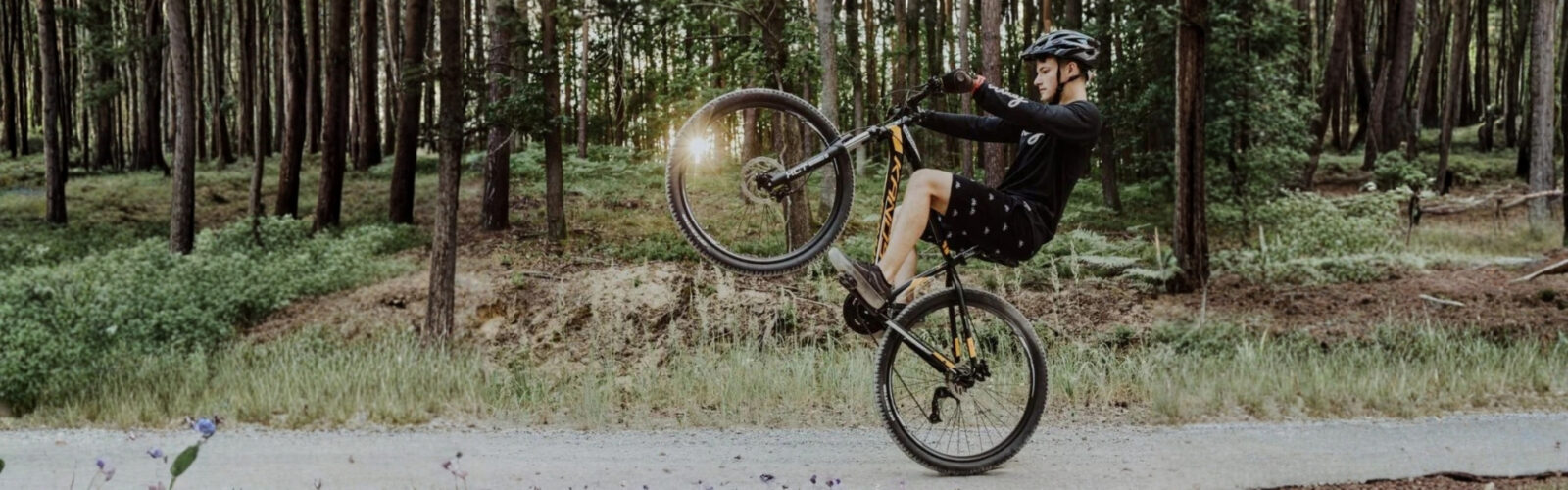 Pyöräilijä temppuilee metsässä kesän auringonlaskussa.